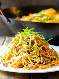 a white plate topped with noodles and meat next to a skillet filled with vegetables