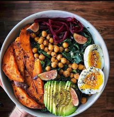 a person holding up a bowl filled with vegetables, eggs and other foods on top of it