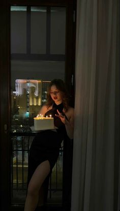 a woman holding a cake with lit candles in her hand while standing next to a window