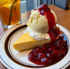 a piece of cheesecake on a plate with ice cream and cherries