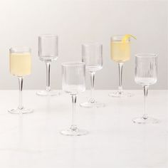 six wine glasses lined up on a white counter top with a lemon wedge in the middle