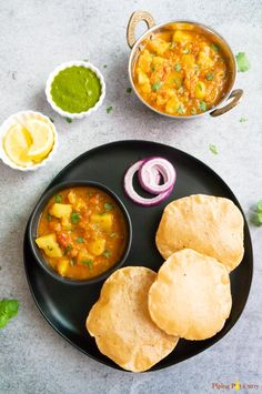 a black plate topped with food next to two bowls of soup and pita bread