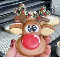 a hand holding up a cookie shaped like a reindeer's head with christmas decorations on it