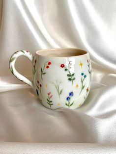 a cup with flowers painted on it sitting on a white cloth covered tablecloth,