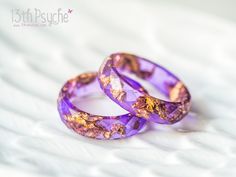 two purple rings sitting on top of a white bed next to each other with gold flakes all over them