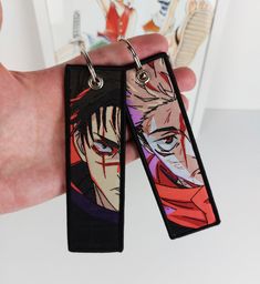 two anime keychains are being held in front of a book with an image of the same character on them