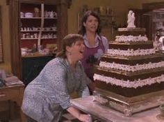 two women standing in front of a large cake on top of a checkered table