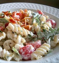 a pasta salad with tomatoes, lettuce and other toppings on a white plate