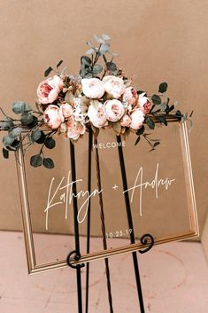 a welcome sign with flowers and greenery is displayed on a metal easel for an outdoor wedding