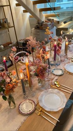 the table is set with plates, candles and flowers in glass vases on it