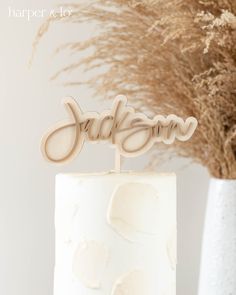 a close up of a white cake with the word jackson on it and flowers in the background