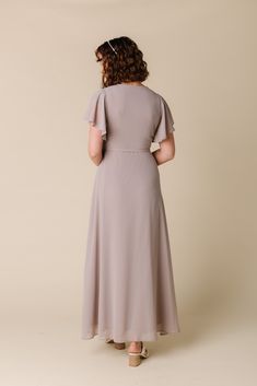 the back view of a woman wearing a grey dress with short sleeves and an open neckline