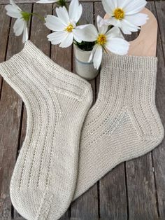 two white socks sitting on top of a wooden table next to flowers and a vase