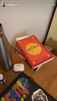 a table topped with books and a metal vase next to it on top of a wooden table