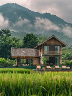 a wooden house sitting in the middle of a lush green field with mountains in the background