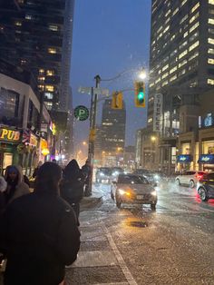 cars driving down a city street in the rain with buildings and traffic lights on either side