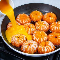 an orange being poured into a pan filled with peeled tangerines on the stove