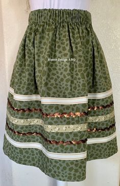 Traditional ribbon skirt in green on green leopard print with elevated details in beige/ivory striped, green floral crossgrain ribbon and brown sequin ribbon lovingly made by hand. A paper bag waist hugs the body, while also being comfortable to wear. See our sizing details below to find your perfect size.  Ready to ship! A long time symbol femininity, sisterhood and solidarity, used in ceremony and everyday, every skirt tells a story written by the woman who wears it. Perfect for every season, dressed up or down. Cross grain and sequin ribbons adorn our skirts and are chosen and arranged by hand during the design process. Each skirt is one of a kind, and may be the only skirt available in the indicated size, fabric, and ribbon combination. Right place, right time? We recommend buying the Ribbon Skirts Native American For Sale, Ribbon Skirts Native American Top, Ribbon Skirts Native American Shirt, Native Print Skirts, Ribbon Skirts Outfit, Ribbon Skirts Native American, Time Symbol, Ribbon Clothes, Skirt Traditional