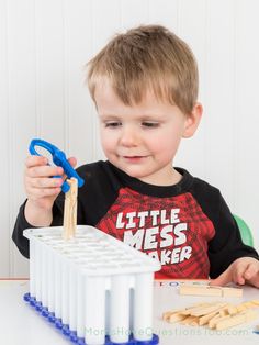 a young boy is playing with wooden pegs and scissors on the table in front of him