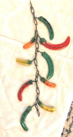 several colorful peppers hang from a metal chain on a piece of white fabric with a black hook