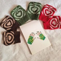 four knitted hand mitts are next to an envelope