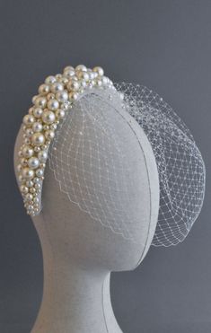 a white headpiece with pearls and netting on it's top, sitting on a mannequin