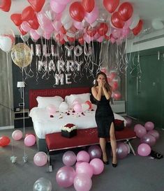 a woman standing in front of a bed surrounded by balloons and streamers, talking on the phone