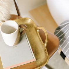 a gold tray with a coffee cup and book on it