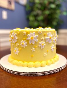 a yellow cake with white and yellow flowers on it sitting on top of a wooden table