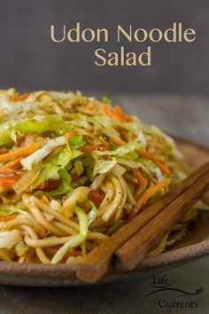 a plate full of noodles and vegetables with chopsticks on the side that says udon noodle salad