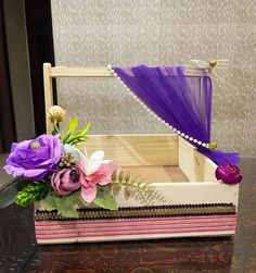 a wooden box with flowers in it sitting on a table next to a purple drape