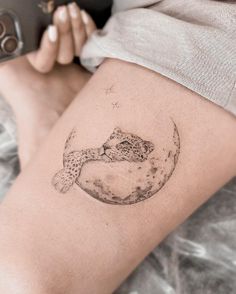 a woman's thigh with a tattoo of a cheetah sitting on the moon