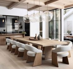 a large wooden table surrounded by white chairs and hanging lights over it's dining room