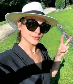 a woman wearing sunglasses and a hat making the peace sign with her hand in front of her