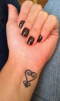 a woman's hand with a heart tattoo on her left wrist and black nail polish