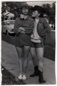 two women standing next to each other on the side of a road with their arms around one another