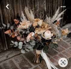 a bridal bouquet with dried flowers and foliage on a brick floor in front of a wooden door