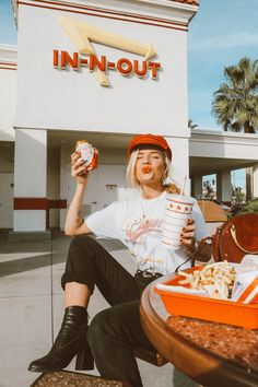 a woman sitting at a table with food in front of a fast food restaurant holding a donut