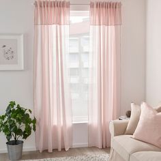 a living room with a couch, chair and window covered in pink drapes next to a potted plant