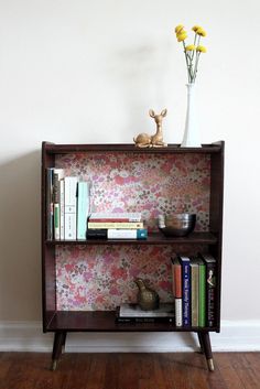 a book shelf with books, vase and flowers on it in front of a white wall