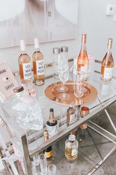 several bottles and glasses on a glass table with a metal tray holding wineglasses