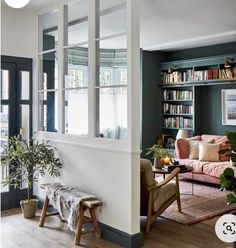 a living room filled with furniture and bookshelves next to a window covered in plants