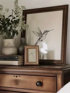 a wooden dresser topped with a clock next to a vase filled with flowers and books