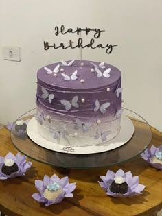 a purple and white cake sitting on top of a wooden table next to paper flowers