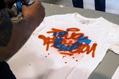 a man is painting a t - shirt with orange and blue spray paint on it