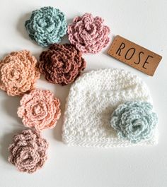 several crocheted flowers and a name tag on a white surface with the word rose written in it