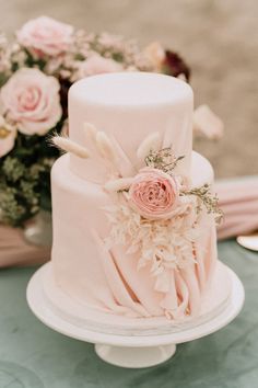 a wedding cake with pink flowers and feathers on the top is sitting on a table