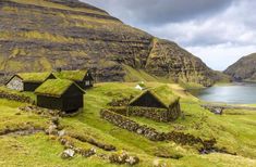 some grass roofed houses are on the side of a hill with water and mountains in the background