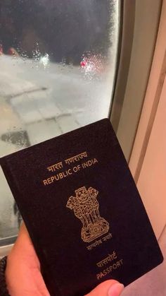 a person holding up a passport in front of a window