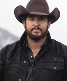 a man with a beard wearing a black shirt and cowboy hat looking at the camera